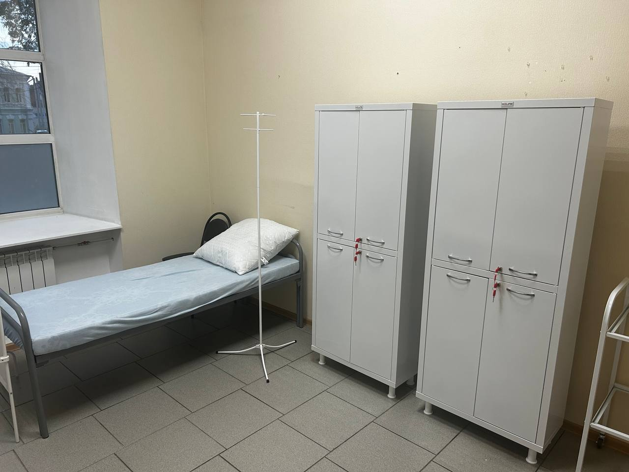 Палата клиники с медицинской кроватью, штативом для капельницы и белыми шкафами