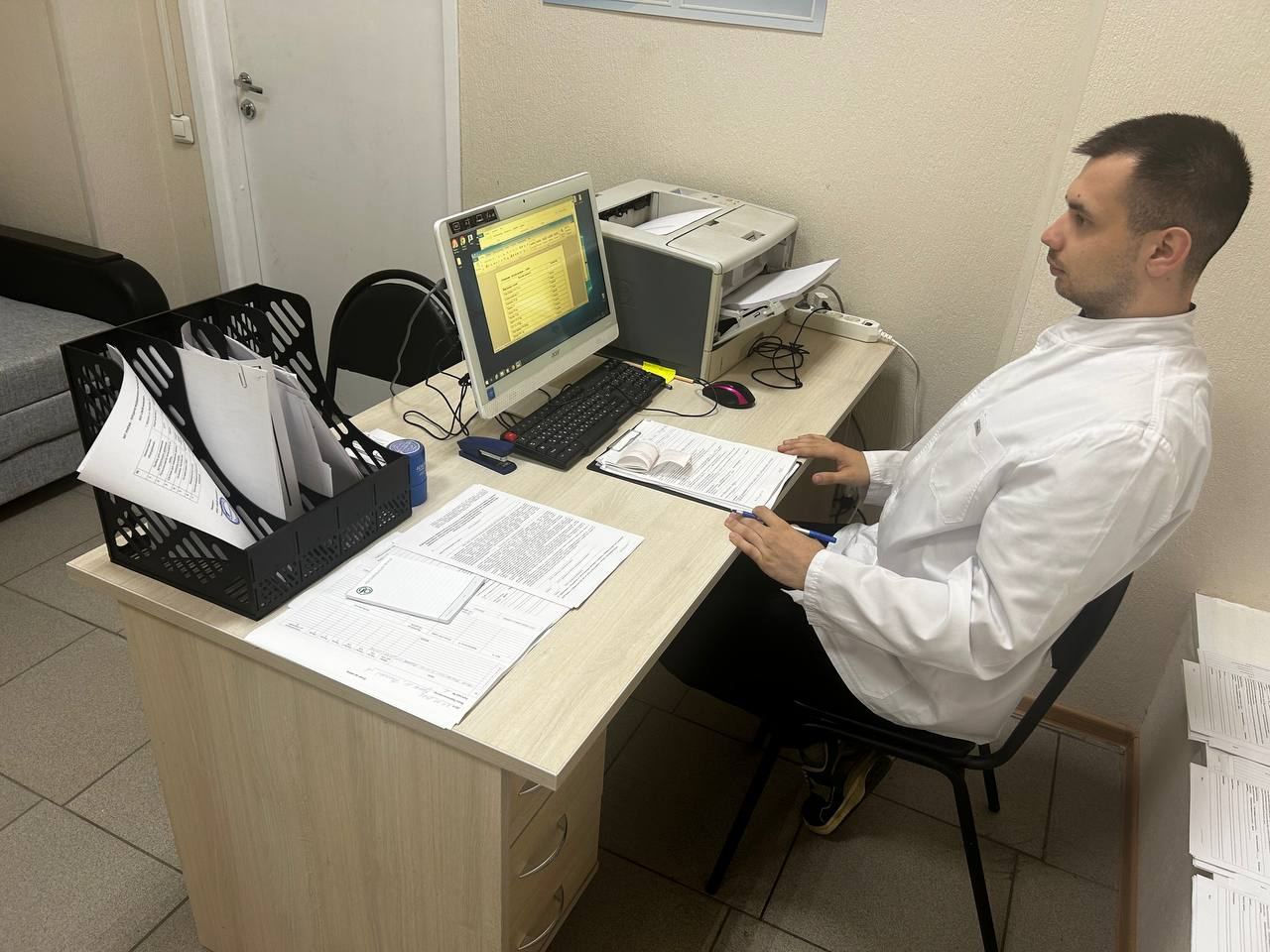 Врач клиники работает за компьютером с документами пациента